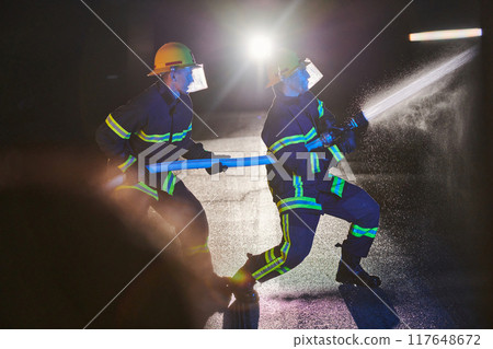 Firefighters using a water hose to eliminate a fire hazard. Team of female and male firemen in dangerous rescue mission.  117648672