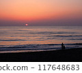Two people on the beach with the sun setting on the horizon 117648683