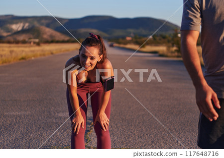A couple resting after a rigorous morning run, embracing the tranquility of their surroundings as they find rejuvenation, fulfillment, and a deep sense of contentment in each other's company 117648716