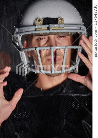American Football Field: Lonely Athlete Warrior Standing on a Field Holds his Helmet and Ready to Play. Player Preparing to Run, Attack and Score Touchdown. Rainy Night with Dramatic Fog, Blue Light 117648736