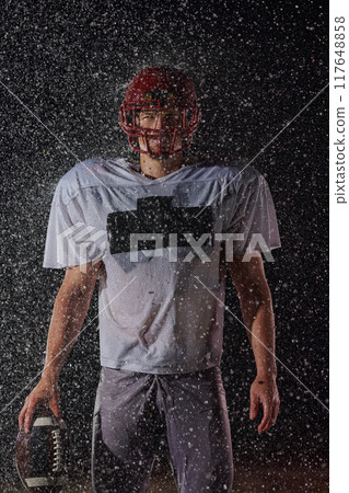 American Football Field: Lonely Athlete Warrior Standing on a Field Holds his Helmet and Ready to Play. Player Preparing to Run, Attack and Score Touchdown. Rainy Night with Dramatic Fog, Blue Light 117648858