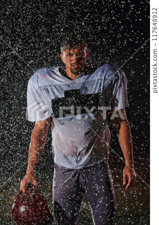 American Football Field: Lonely Athlete Warrior Standing on a Field Holds his Helmet and Ready to Play. Player Preparing to Run, Attack and Score Touchdown. Rainy Night with Dramatic Fog, Blue Light 117648912