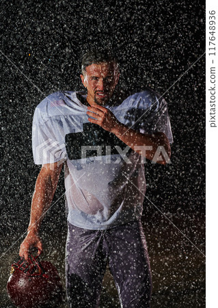 American Football Field: Lonely Athlete Warrior Standing on a Field Holds his Helmet and Ready to Play. Player Preparing to Run, Attack and Score Touchdown. Rainy Night with Dramatic Fog, Blue Light 117648936