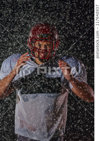 American Football Field: Lonely Athlete Warrior Standing on a Field Holds his Helmet and Ready to Play. Player Preparing to Run, Attack and Score Touchdown. Rainy Night with Dramatic Fog, Blue Light 117648937