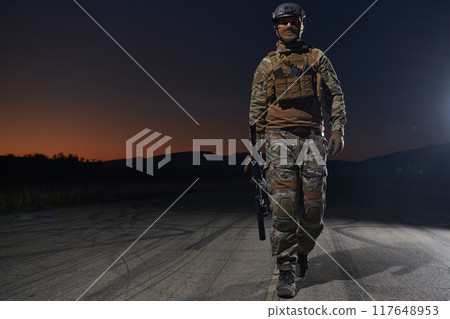 A professional soldier in full military gear striding through the dark night as he embarks on a perilous military mission 117648953