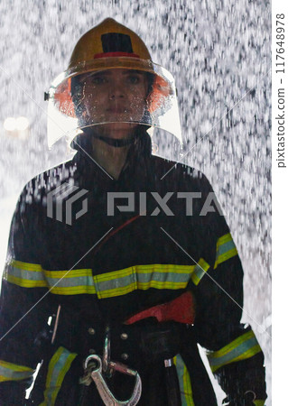 A determined female firefighter in a professional uniform striding through the dangerous, rainy night on a daring rescue mission, showcasing her unwavering bravery and commitment to saving lives. A determined female firefighter in a professional uniform striding through the dangerous, rainy night on a daring rescue mission, showcasing her unwavering bravery and commitment to saving lives. 117648978