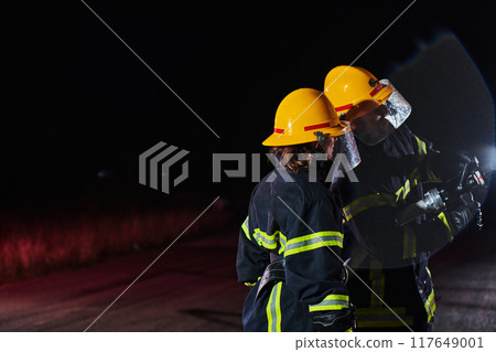 Firefighters using a water hose to eliminate a fire hazard. Team of female and male firemen in dangerous rescue mission. Firefighters using a water hose to eliminate a fire hazard. Team of female and male firemen in dangerous rescue mission. 117649001
