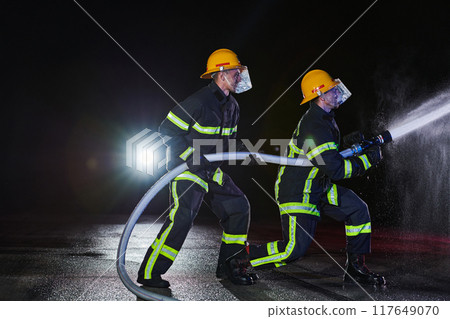 Firefighters using a water hose to eliminate a fire hazard. Team of female and male firemen in dangerous rescue mission. Firefighters using a water hose to eliminate a fire hazard. Team of female and male firemen in dangerous rescue mission. 117649070
