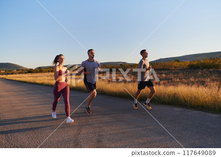 A group of young athletes running together in the early morning light of the sunrise, showcasing their collective energy, determination, and unity A group of young athletes running together in the early morning light of the sunrise, showcasing their collective energy, determination, and unity 117649089