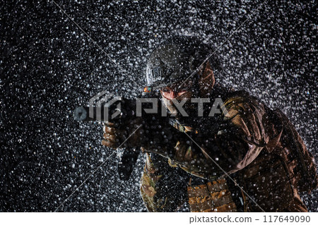 Army soldier in Combat Uniforms with an assault rifle, plate carrier and combat helmet going on a dangerous mission on a rainy night. 117649090