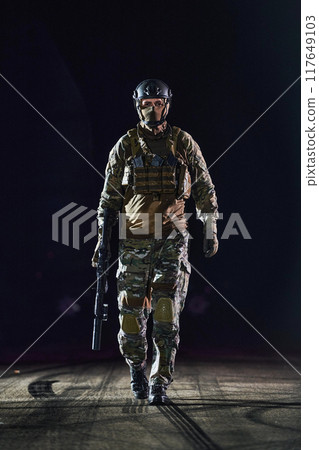 A professional soldier in full military gear striding through the dark night as he embarks on a perilous military mission 117649103