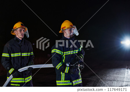 Firefighters using a water hose to eliminate a fire hazard. Team of female and male firemen in dangerous rescue mission. Firefighters using a water hose to eliminate a fire hazard. Team of female and male firemen in dangerous rescue mission. 117649171