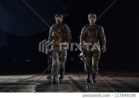 Two professional soldiers marching through the dark of night on a dangerous mission, epitomizing their unwavering bravery, unwavering teamwork, and the high-stakes intensity of their specialized 117649198