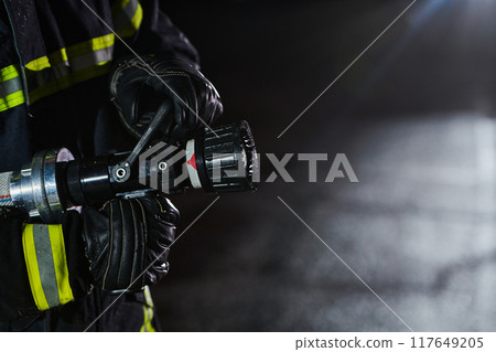 Firefighter using a water hose to eliminate a fire hazard. Team of firemen in the dangerous rescue mission. 117649205