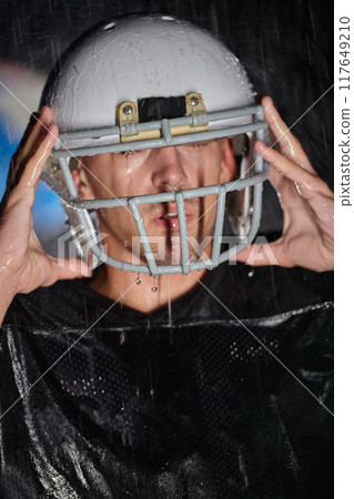 American Football Field: Lonely Athlete Warrior Standing on a Field Holds his Helmet and Ready to Play. Player Preparing to Run, Attack and Score Touchdown. Rainy Night with Dramatic Fog, Blue Light American Football Field: Lonely Athlete Warrior Standing on a Field Holds his Helmet and Ready to Play. Player Preparing to Run, Attack and Score Touchdown. Rainy Night with Dramatic Fog, Blue Light 117649210
