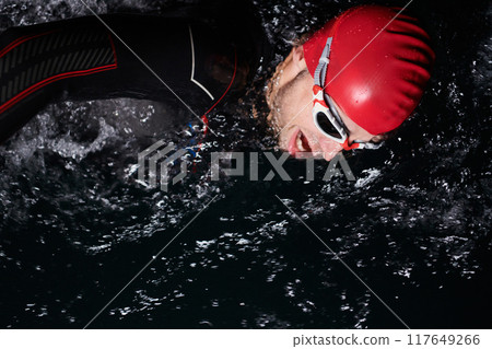 A determined professional triathlete undergoes rigorous night time training in cold waters, showcasing dedication and resilience in preparation for an upcoming triathlon swim competition A determined professional triathlete undergoes rigorous night time training in cold waters, showcasing dedication and resilience in preparation for an upcoming triathlon swim competition 117649266