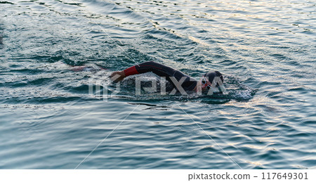A professional triathlete trains with unwavering dedication for an upcoming competition at a lake, emanating a sense of athleticism and profound commitment to excellence. 117649301