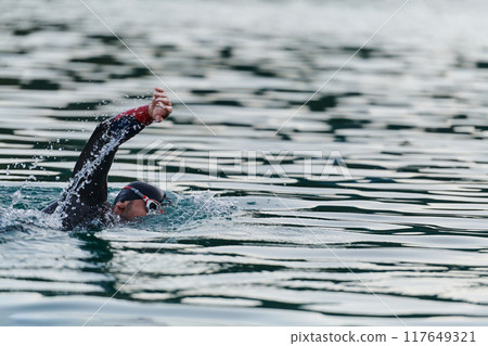 A professional triathlete trains with unwavering dedication for an upcoming competition at a lake, emanating a sense of athleticism and profound commitment to excellence. A professional triathlete trains with unwavering dedication for an upcoming competition at a lake, emanating a sense of athleticism and profound commitment to excellence. 117649321