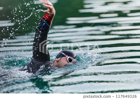 A professional triathlete trains with unwavering dedication for an upcoming competition at a lake, emanating a sense of athleticism and profound commitment to excellence. 117649326