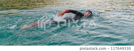 A professional triathlete trains with unwavering dedication for an upcoming competition at a lake, emanating a sense of athleticism and profound commitment to excellence. 117649330