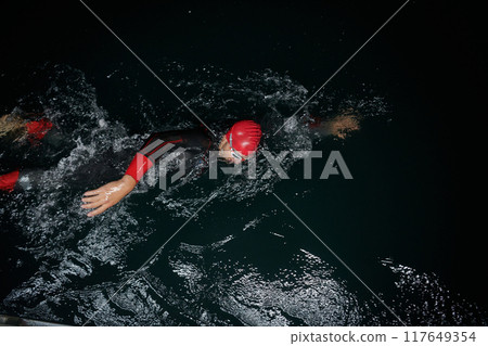 A determined professional triathlete undergoes rigorous night time training in cold waters, showcasing dedication and resilience in preparation for an upcoming triathlon swim competition 117649354