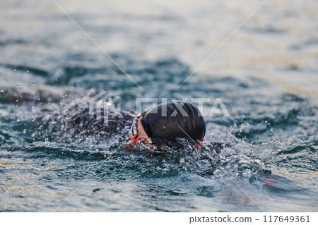 A professional triathlete trains with unwavering dedication for an upcoming competition at a lake, emanating a sense of athleticism and profound commitment to excellence. 117649361