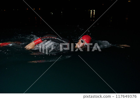 A determined professional triathlete undergoes rigorous night time training in cold waters, showcasing dedication and resilience in preparation for an upcoming triathlon swim competition 117649376