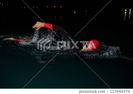 A determined professional triathlete undergoes rigorous night time training in cold waters, showcasing dedication and resilience in preparation for an upcoming triathlon swim competition 117649379