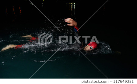 A determined professional triathlete undergoes rigorous night time training in cold waters, showcasing dedication and resilience in preparation for an upcoming triathlon swim competition A determined professional triathlete undergoes rigorous night time training in cold waters, showcasing dedication and resilience in preparation for an upcoming triathlon swim competition 117649381