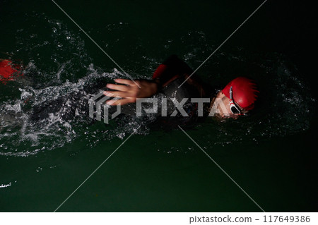 A determined professional triathlete undergoes rigorous night time training in cold waters, showcasing dedication and resilience in preparation for an upcoming triathlon swim competition 117649386