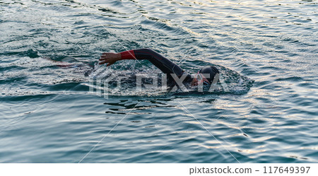 A professional triathlete trains with unwavering dedication for an upcoming competition at a lake, emanating a sense of athleticism and profound commitment to excellence. 117649397