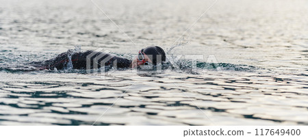 A professional triathlete trains with unwavering dedication for an upcoming competition at a lake, emanating a sense of athleticism and profound commitment to excellence. 117649400