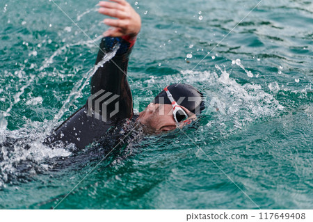 A professional triathlete trains with unwavering dedication for an upcoming competition at a lake, emanating a sense of athleticism and profound commitment to excellence. 117649408