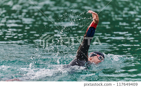 A professional triathlete trains with unwavering dedication for an upcoming competition at a lake, emanating a sense of athleticism and profound commitment to excellence. 117649409