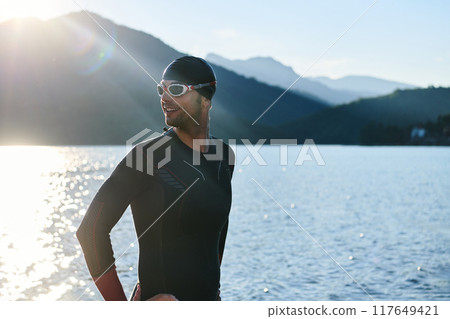 Authentic triathlon athlete getting ready for swimming training on lake 117649421