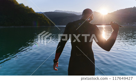 Authentic triathlon athlete getting ready for swimming training on lake Authentic triathlon athlete getting ready for swimming training on lake 117649427