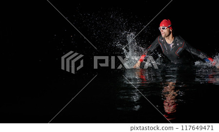 A determined professional triathlete undergoes rigorous night time training in cold waters, showcasing dedication and resilience in preparation for an upcoming triathlon swim competition 117649471