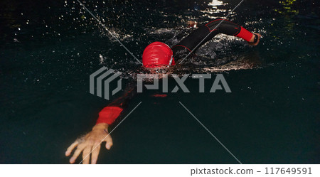 A determined professional triathlete undergoes rigorous night time training in cold waters, showcasing dedication and resilience in preparation for an upcoming triathlon swim competition 117649591