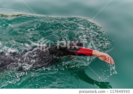 A professional triathlete trains with unwavering dedication for an upcoming competition at a lake, emanating a sense of athleticism and profound commitment to excellence. 117649593