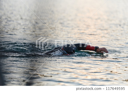 A professional triathlete trains with unwavering dedication for an upcoming competition at a lake, emanating a sense of athleticism and profound commitment to excellence. 117649595