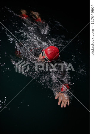 A determined professional triathlete undergoes rigorous night time training in cold waters, showcasing dedication and resilience in preparation for an upcoming triathlon swim competition 117649604