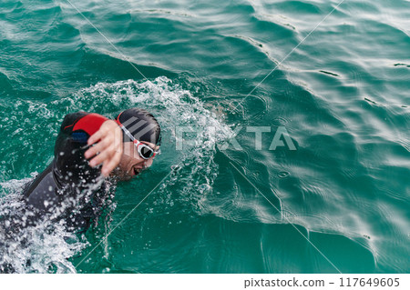 A professional triathlete trains with unwavering dedication for an upcoming competition at a lake, emanating a sense of athleticism and profound commitment to excellence. 117649605