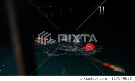 A determined professional triathlete undergoes rigorous night time training in cold waters, showcasing dedication and resilience in preparation for an upcoming triathlon swim competition 117649638
