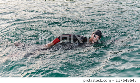 A professional triathlete trains with unwavering dedication for an upcoming competition at a lake, emanating a sense of athleticism and profound commitment to excellence. 117649645