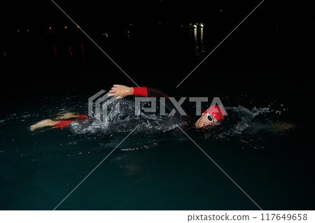 A determined professional triathlete undergoes rigorous night time training in cold waters, showcasing dedication and resilience in preparation for an upcoming triathlon swim competition 117649658