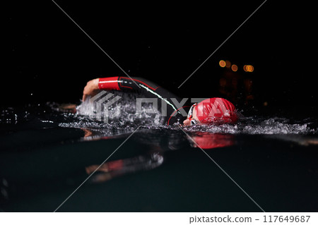 A determined professional triathlete undergoes rigorous night time training in cold waters, showcasing dedication and resilience in preparation for an upcoming triathlon swim competition 117649687