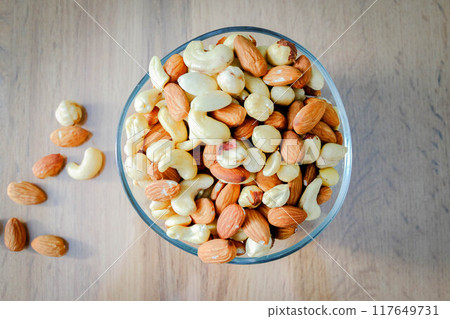 Cashews, peanuts and almonds on a plate. Nuts on the table in the bright rays of the sun. Cashews, peanuts and almonds on a plate. Nuts on the table in the bright rays of the sun. 117649731
