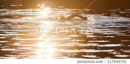 Triathlon athlete swimming on lake in sunrise wearing wetsuit 117649781