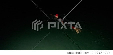 A determined professional triathlete undergoes rigorous night time training in cold waters, showcasing dedication and resilience in preparation for an upcoming triathlon swim competition A determined professional triathlete undergoes rigorous night time training in cold waters, showcasing dedication and resilience in preparation for an upcoming triathlon swim competition 117649798