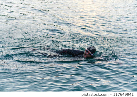 A professional triathlete trains with unwavering dedication for an upcoming competition at a lake, emanating a sense of athleticism and profound commitment to excellence. 117649941